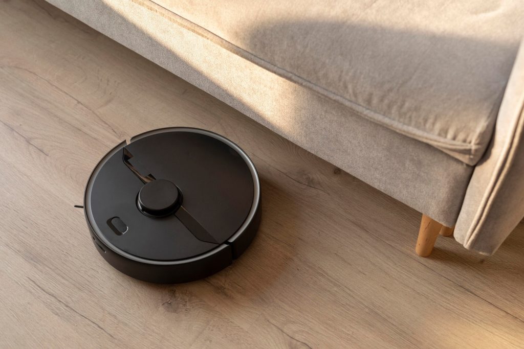 Svart robotdammsugare på trägolvet intill en ljusgrå soffa